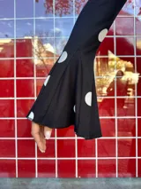 Blusa negra con estampado de lunares blancos, de corte ajustado al cuerpo, cuello redondo y mangas largas con terminación acampanada.