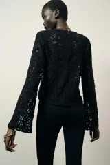 Top de encaje negro con cuello redondo, manga larga y hombreras incorporadas. Presenta un diseño de corte recto y cierre posterior.