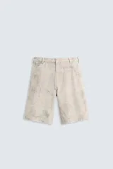 Bermuda de algodón color beige claro con efecto lavado y estampado abstracto en tonos grises. Diseño de corte relajado con cierre frontal de botón y cremallera, bolsillos delanteros y bolsillos traseros de plastrón.