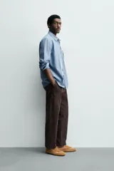 Camisa de corte regular fit confeccionada en tejido chambray de algodón con efecto lavado. Presenta cuello con botones, manga larga con puños abotonados, bolsillo en el pecho y cierre frontal de botones.