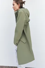 Chubasquero verde militar de cuello subido con capucha ajustable con cordones. Tiene manga larga, bolsillos delanteros con solapa y botón a presión oculto, y cierre frontal con cremallera oculta y botones a presión.