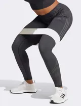 Calza deportiva Adidas Seamless 7/8 de tiro alto, color negro, confeccionada con tejido suave y elástico sin costuras con tecnología AEROREADY. Presenta diseño de líneas acanaladas en la cintura y los tobillos, y las tres tiras características de la marca en el muslo derecho.
