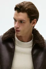 Campera de tejido revestido con acabado efecto cuero envejecido, cuello de solapa con forro de sherpa, cierre frontal y bolsillos laterales con cierre.
