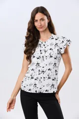 Blusa blanca sin mangas con volados en los hombros, cuello redondo con aberturas y cierre frontal parcial con botones.
