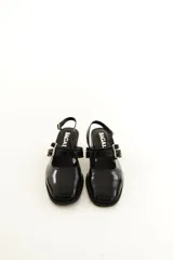 Zapatos tipo Mary Jane de charol color negro, con taco bloque, talón descubierto y doble tira frontal con hebillas metálicas.