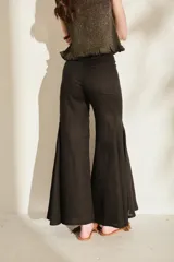 Pantalón negro de lino de tiro alto, con diseño ajustado en las caderas y perneras amplias y acampanadas con paneles insertados que generan mucho vuelo en el bajo.