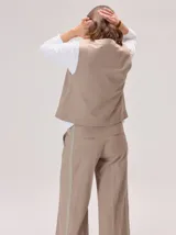 Chaleco negro sin mangas, de corte recto y largo a la cintura, con cuello redondo y cierre frontal oculto.