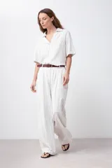 Pantalón de lino color blanco con finas rayas verticales negras, corte palazzo, cintura alta con pinzas y cinturón marrón.