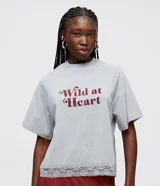 Remera gris melange de media malla con cuello redondo, mangas cortas raglán y estampado "Wild at Heart" en color bordó. El bajo de la remera cuenta con una aplicación de encaje.