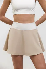Pollera deportiva de corte acampanado color beige, con calza corta integrada de color blanco. Presenta cintura ancha de tiro alto y bolsillo invertido en la calza para guardar pelotas.