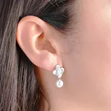 Aros colgantes plateados con forma de flor de cuatro pétalos, decorados con pequeñas circonias y una perla colgante.