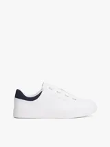 Zapatillas de tenis minimalistas Tommy Hilfiger, confeccionadas en piel napa blanca con suela gruesa tipo cupsole. Presentan un diseño de corte bajo con cordones, detalle de panel azul marino en el talón y logo metálico de la marca en el lateral.