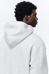 Campera con capucha en felpa de peso medio color gris claro, con interior cepillado suave, cierre y bolsillos delanteros, puños y bajo en punto acanalado. Corte holgado.