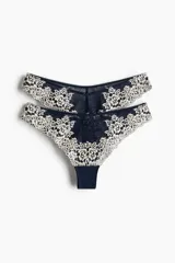 Pack de dos bombachas tipo brazilian de tiro bajo, confeccionadas en encaje floral bicolor azul marino y crema con detalles de malla y pequeño lazo decorativo en el centro.