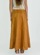 Pollera larga de lino color blanco, con corte acampanado y paneles verticales con costuras a la vista.