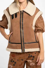 Chaleco estilo gamulán de color negro, con interior y cuello de corderito sintético. Presenta cierre frontal, detalles en cuero sintético y corte oversize.