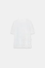 Camiseta de algodón de corte regular, con cuello redondo y manga corta. Presenta un detalle decorativo de flores con volumen confeccionadas en el mismo tejido sobre el frente.