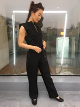 Mono largo de lino color beige, con detalle plisado en el frente, escote en V, sin mangas, lazo en la cintura, cierre invisible delantero y bolsillos laterales.