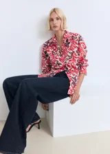 Camisa de corte recto y diseño holgado, confeccionada en algodón con estampado floral en tonos rojos y bordó sobre fondo crudo. Presenta cuello camisero clásico, cierre frontal con botones y mangas largas.