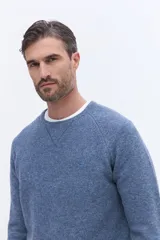 Sweater de tejido suave color azul jaspeado, con cuello redondo, mangas raglán y detalle de costura triangular en el escote. Presenta un pequeño logo bordado en el pecho.