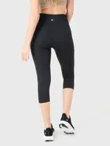 Calza deportiva tipo capri de tiro alto, color negro, con pretina elástica reforzada y detalle de logo pequeño en la cadera.