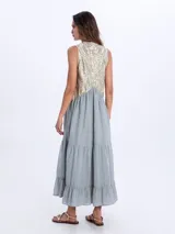 Vestido largo sin mangas, de color negro con la parte superior bordada en tonos dorados y negros con patrones geométricos. Presenta escote en V y falda con volados escalonados.