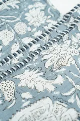 Bolso tipo tote bag de tela acolchada con estampado floral en tonos gris y blanco. Presenta asas largas reforzadas con detalle de rayas en los bordes.