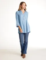 Blusa de lyocell color azul claro, con cuello camisero, escote en V y cierre frontal parcial con botones. Presenta mangas tres cuartos amplias y un corte holgado con aberturas laterales en el ruedo.