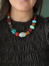 Collar corto de diseño artesanal compuesto por una variedad de cuentas de diferentes materiales, formas y colores, incluyendo cerámica, acrílico y piedras. Cuenta con un cierre de cadena de acero quirúrgico ajustable.