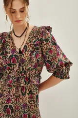 Vestido midi de algodón con estampado floral y geométrico en tonos tierra, fucsia y verde. Presenta escote en V, mangas abullonadas con volados en los hombros y falda con volados en el ruedo.