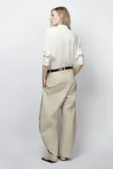 Camisa fluida de cuello redondo y manga larga con puños. Presenta un diseño con pechera frontal, cierre con botones y bajo asimétrico redondeado.