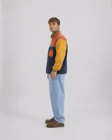 Buzo polar de hombre con diseño color block en tonos azul marino, amarillo y naranja. Cuenta con cuello alto con cierre de botones a presión, bolsillo frontal con solapa y cierre, y mangas largas con puños elásticos.