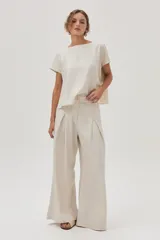 Pantalón de lino color beige, de pierna ancha, con botón en la cintura, pinzas en el frente y bolsillos delanteros y traseros.