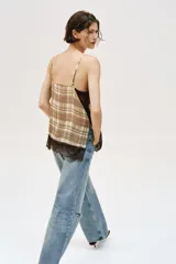 Top lencero de escote en pico con tirantes finos ajustables. Presenta un estampado de cuadros en tonos beige y marrón, con detalles de encaje negro en el escote y en el ruedo.