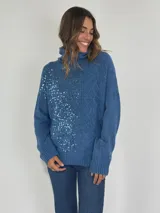 Sweater azul de tejido de punto con cuello alto y apliques de lentejuelas en el frente.