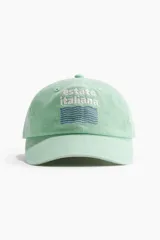 Gorra de sarga de algodón verde menta con visera curva y cierre ajustable con hebilla metálica en la parte trasera. Cuenta con bordado frontal con el texto "estate italiana" y diseño de ondas.