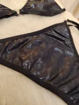 Conjunto de bikini negro de cuerina texturizada, con corpiño triangular con aro metálico central y bombacha colaless con tiras laterales ajustables.