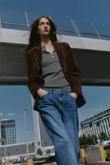 Blazer de piel 100% color marrón oscuro, con cuello solapa, manga larga con hombreras y bolsillos delanteros con solapa. Presenta pespuntes decorativos en contraste y cierre frontal con un botón.