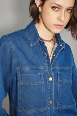 Camisa crop de denim azul, con cuello camisero, botones frontales dorados, dos bolsillos en el pecho y mangas abullonadas.