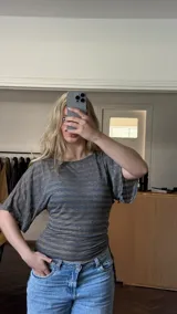 Remera de manga corta gris con rayas horizontales doradas y brillo, ajustada en la cintura con frunce regulable en el lado derecho.