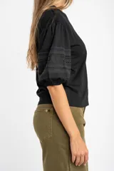 Remera negra de algodón con mangas cortas abullonadas que presentan detalles de encaje bordado y calado en los extremos.