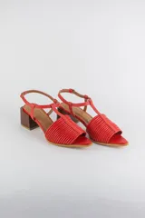 Sandalias de cuero rojo con diseño de tiras horizontales abullonadas en la parte delantera, punta fina, tira vertical central en forma de T y tira ajustable al tobillo. Poseen tacón cuadrado de madera de 6 cm.