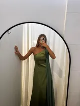 Vestido largo de tafeta con brillo, color verde, de corte al cuerpo y escote asimétrico de un solo hombro. Incluye una pieza de seda liviana drapeada sobre el hombro opuesto.