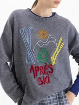Sweater de lana gris con silueta holgada y cuello redondo. Presenta un bordado frontal colorido con motivos de esquí y la inscripción 'Apres Ski'.