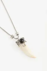 Collar largo de estilo boho con cadena metálica, cuentas de vidrio y dije central con forma de colmillo y piedra oscura.