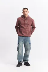 Canguro con capucha y cordones ajustables, confeccionado en algodón color bordó. Presenta un bolsillo frontal tipo canguro, puños y ruedo acanalados, y un estampado gráfico pequeño en el pecho con la frase 'Your smile is eternal'.