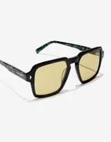 Lentes de sol Hawkers modelo Lash con armazón negro de frente cuadrado y patillas con estampado de mármol en tonos verdes. Presentan cristales amarillos y detalles metálicos en las esquinas.