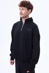 Buzo de felpa color negro con cuello alto y cierre frontal parcial. Presenta un diseño holgado con bolsillos laterales y logo bordado en el pecho.