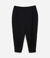 Pantalón zanahoria de vestir negro, con cintura alta, elástico en la espalda, bolsillos laterales, botón metalizado y pliegues delanteros.