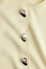 Chaleco color crema con cuello redondo y cierre frontal con botones metálicos.